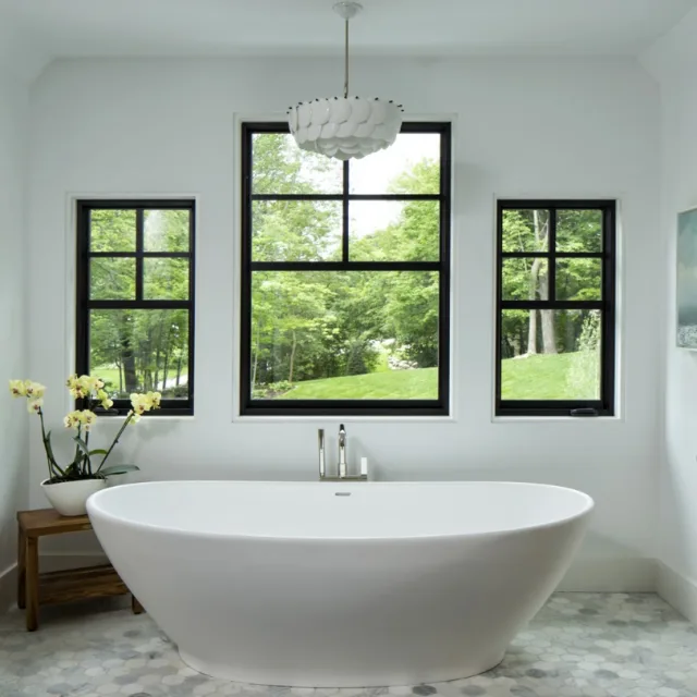 A bright bathroom with three black framed windows behind a freestanding tub