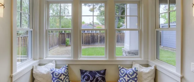 A bay window seat with blue and white cushions below a run of double hung windows