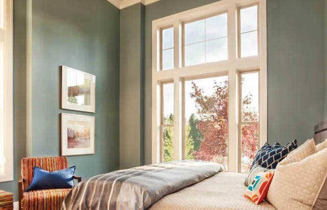 A bedroom with tall windows and upper transoms looking out at autumn trees