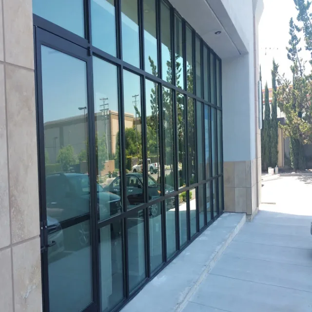 A tall wall of black framed storefront glass along a concrete walkway, reflecting a parking lot