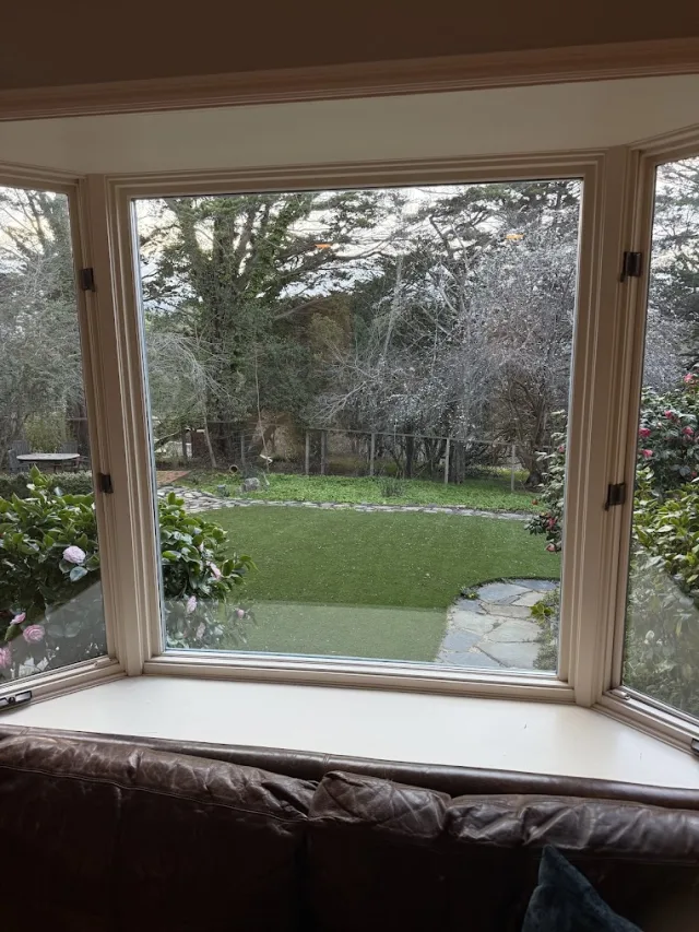 A bay window with clear glass looking out onto a garden and lawn