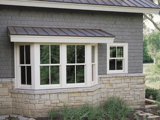 A craftsman style house with a white bay window above a stone base and a small metal roof