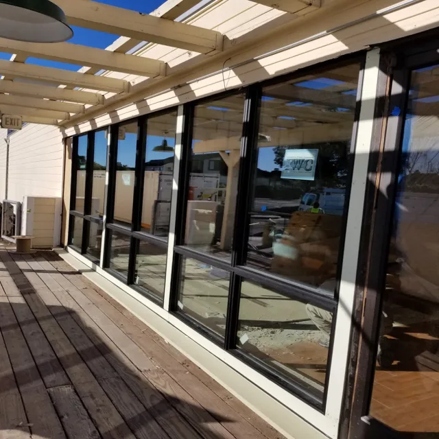 A row of black framed windows along a wooden deck under a pergola