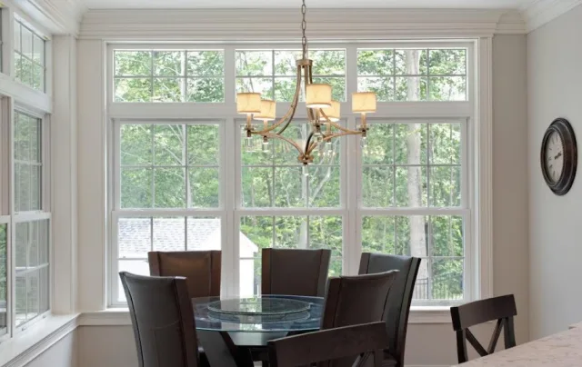 A dining room with a round glass table, a brass chandelier and tall double hung windows