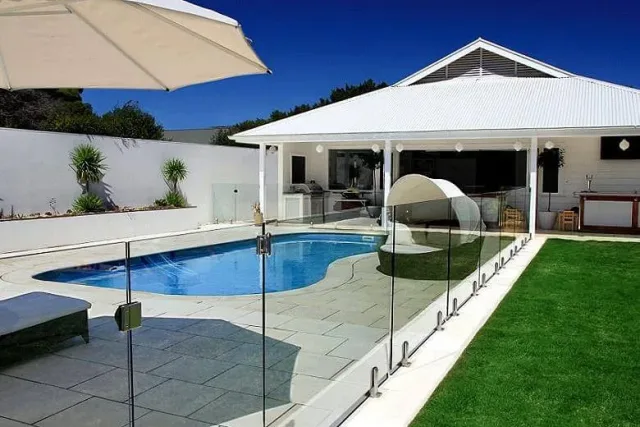 Frameless glass pool fencing on a stone patio beside a curved pool and a white pavilion