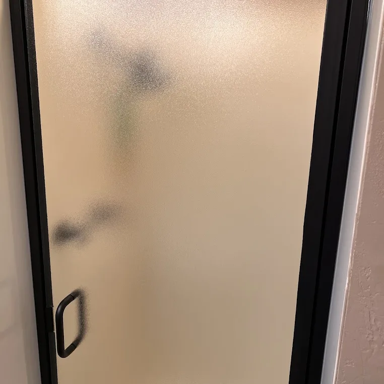 A frosted glass shower door with a slim black frame and a black handle