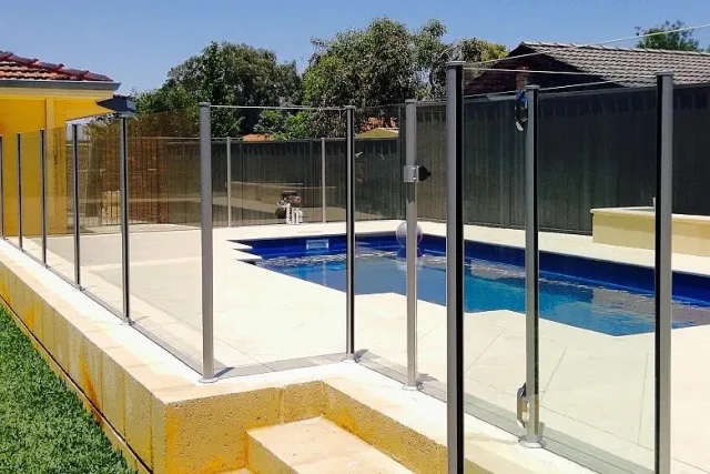 A glass pool fence with slim aluminum posts around an in ground pool and steps