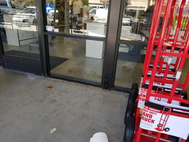 Dark framed glass entry doors at a hardware store, with red hand trucks on display beside them