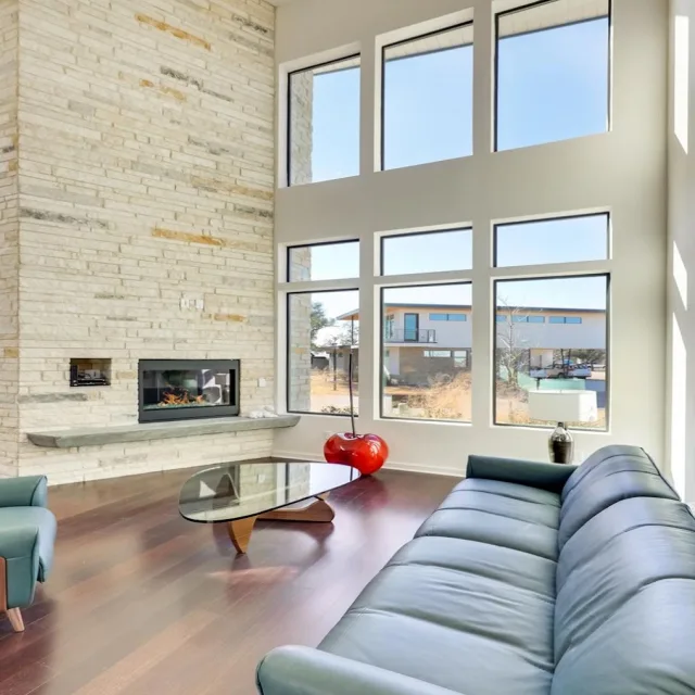 A tall living room with stacked windows beside a stone fireplace wall and a blue sofa
