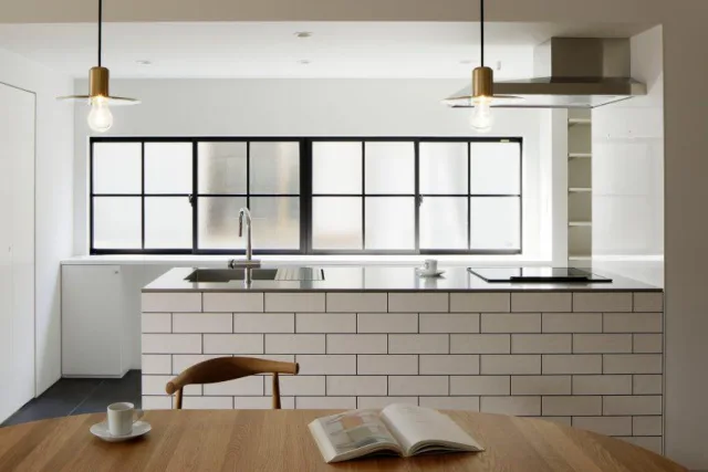 A white kitchen with a long black framed window above a tiled island and sink