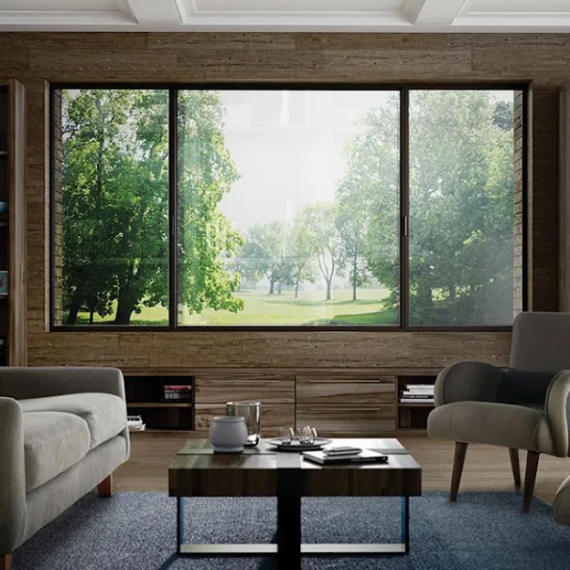 A living room with a wide dark framed picture window looking out onto a park with trees