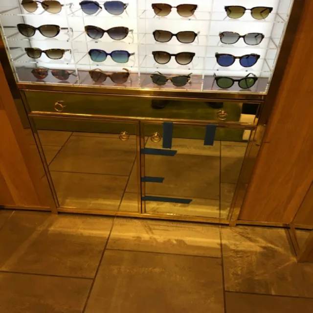 A tall retail display cabinet with glass doors and glass shelves holding rows of sunglasses