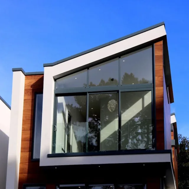A modern home with a large angled glass facade framed in white panels and wood cladding