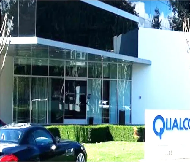 A two story office building with a glass curtain wall and a glass entrance behind a trimmed hedge