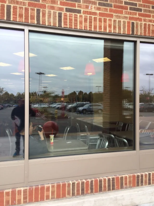 A tall storefront window above a brick base, reflecting a parking lot, with cafe tables inside