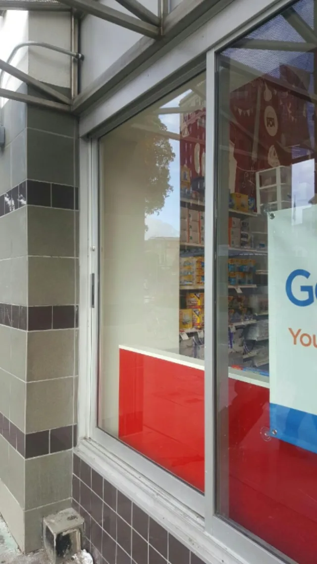 A tall aluminum framed side window beside a store entrance, with tile trim and a sign inside