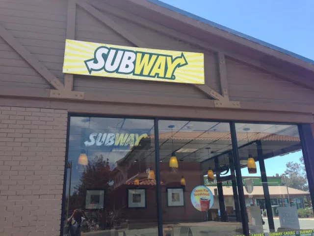 The storefront windows of a sandwich shop under its sign, with a covered walkway at one side
