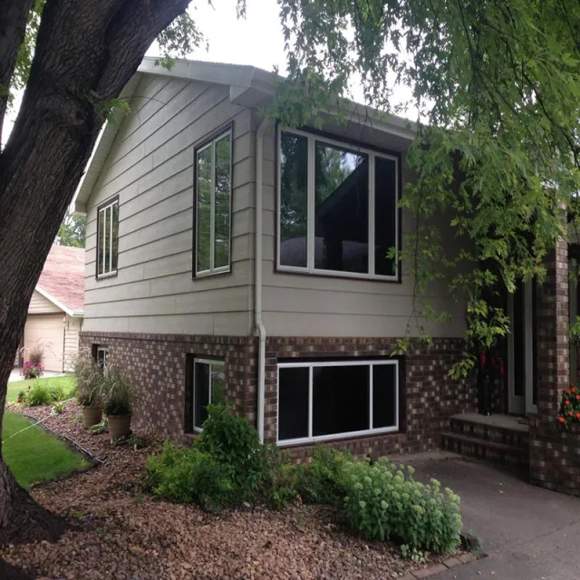 A split level home with dark framed windows on the upper floor and a wide window at the brick lower level