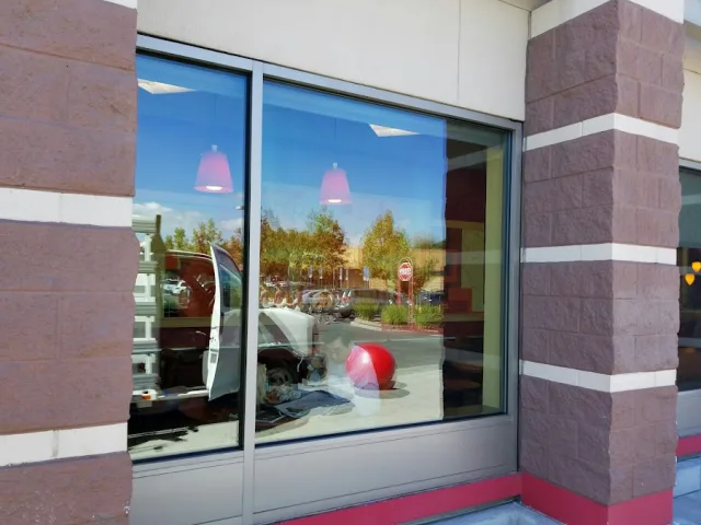 A wide two pane storefront window set between red brick pillars, reflecting cars and trees