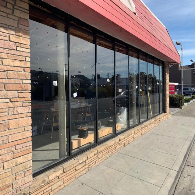 A long run of dark framed storefront windows above a brick base, under a red roof edge