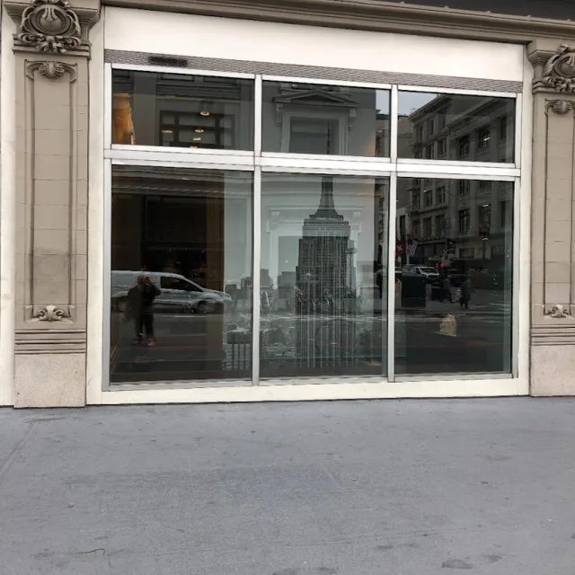 A storefront window of three large panes and three transom panes set into a carved stone building front