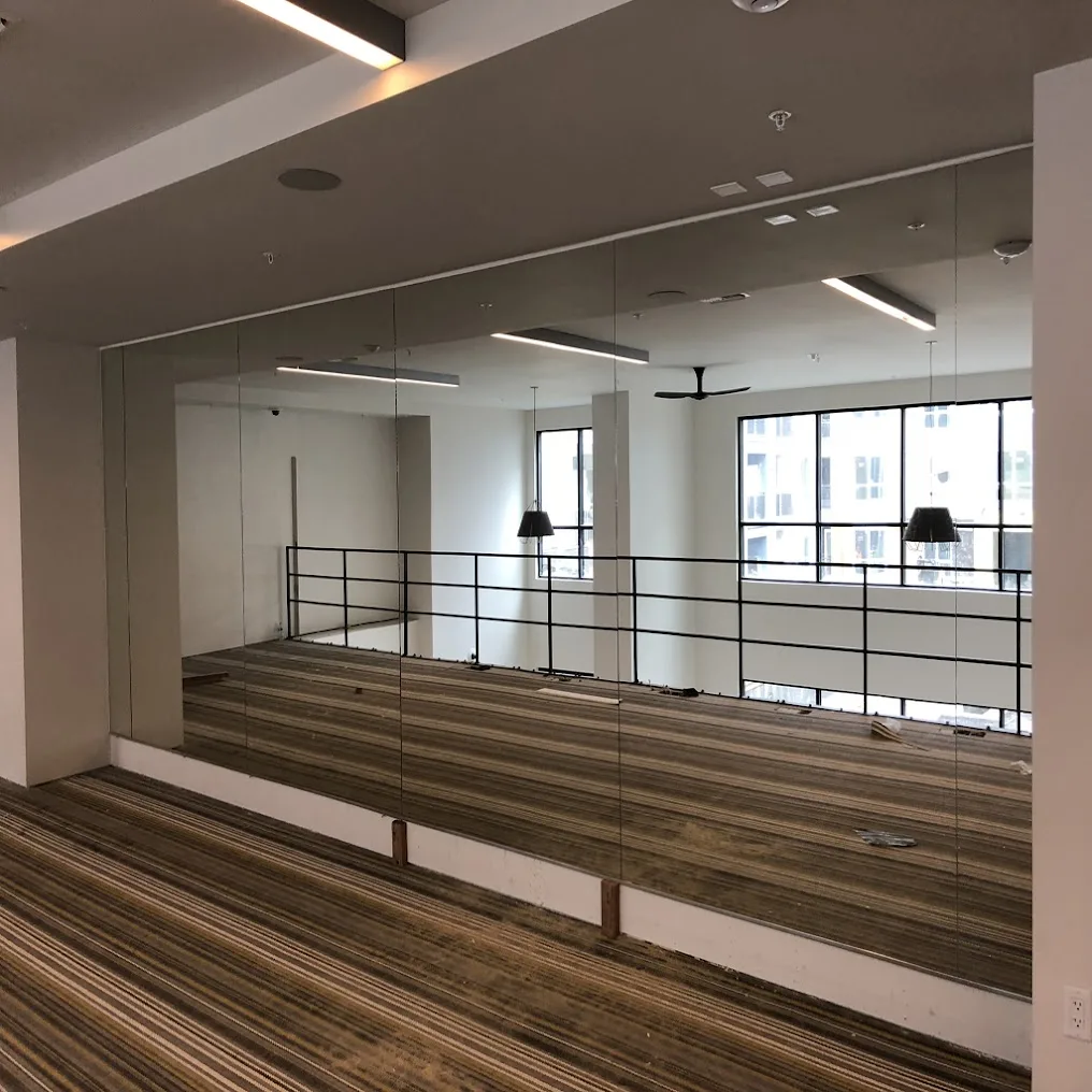 A full wall of mirrors in an open studio with a wood floor and a railing along a raised level