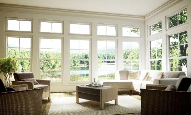 A sunroom with walls of white framed windows and transoms looking out at a lake