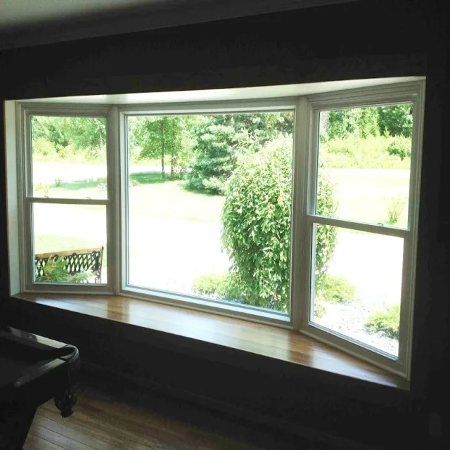A bay window with three lites and a wide wood sill, looking out onto a green yard