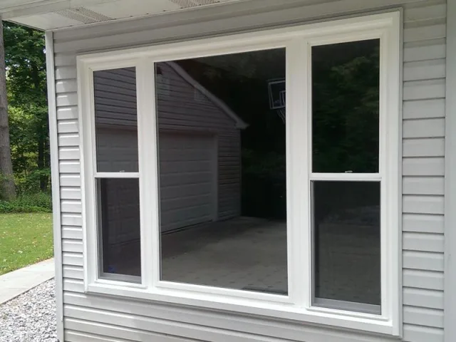 A white vinyl window with a large center pane and a double hung window on each side, set in white siding