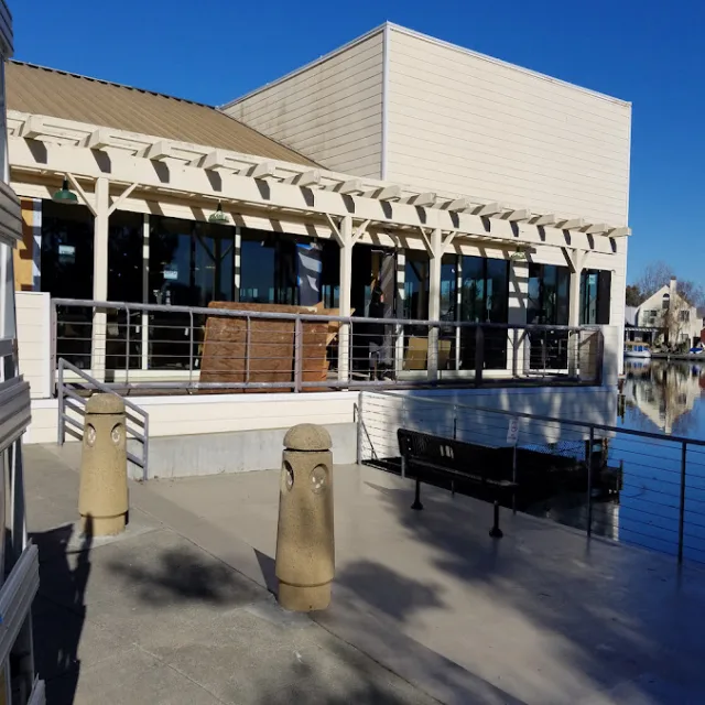 A waterfront building with a pergola covered patio, glass across the front and a railing along the water