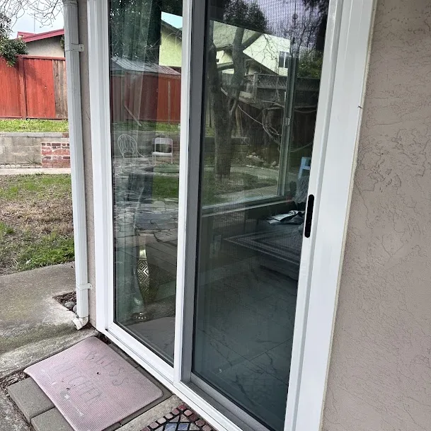 A white vinyl sliding patio door seen from the side, with a doormat on the step below it