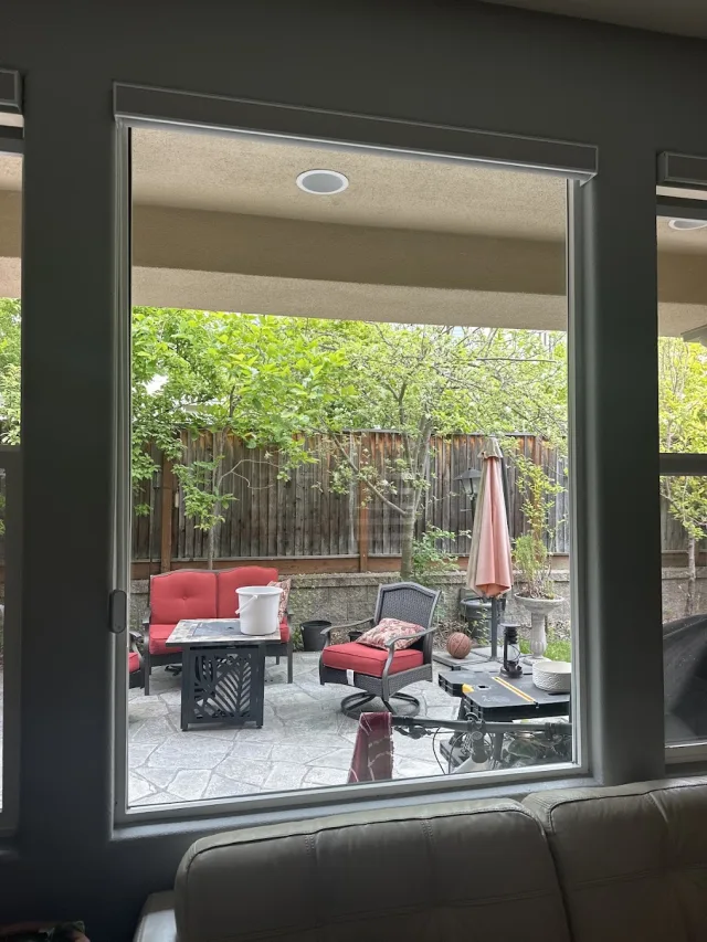 A large window with a dark frame looking out onto a backyard patio with red cushions